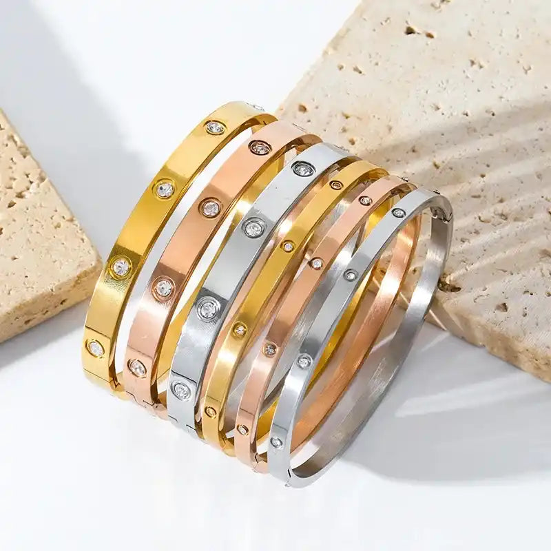 Stacked metallic bangles in gold, rose gold, and silver tones with embedded crystals.