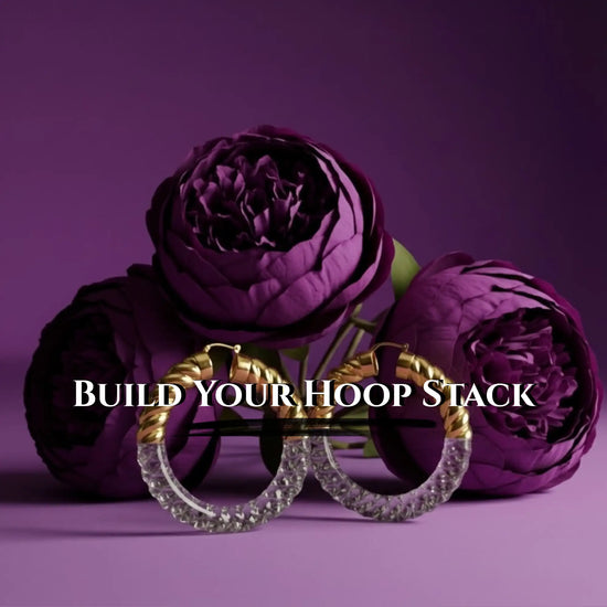 Gold and clear crystal hoop earrings with a twisted design, displayed against deep purple peonies.