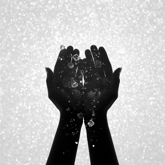 Silhouetted hands catching falling water droplets.