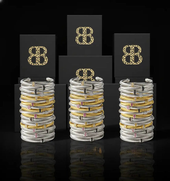 Stacks of silver and gold-toned cable bracelets with embedded pink gemstones, presented in elegant black boxes bearing the brand’s distinctive logo.