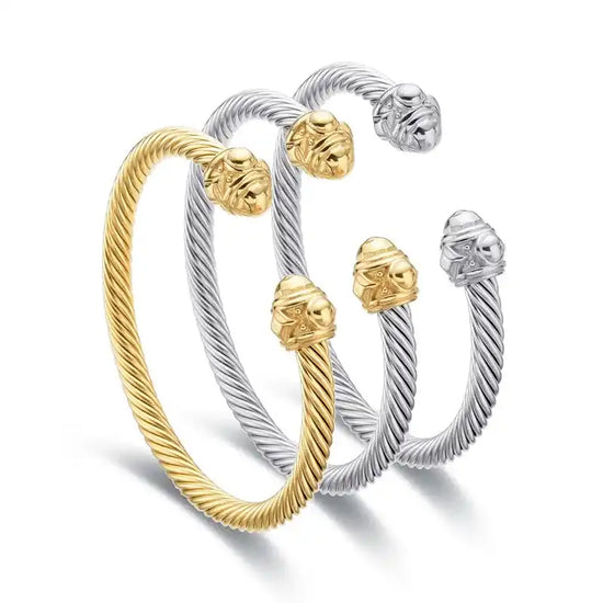 Three twisted cable bracelets, two silver-toned with gold-toned finials and one entirely gold-toned, each featuring decorative lion head ends.