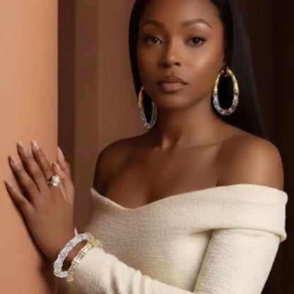 Woman wearing a beige off-shoulder top with jewelry against a neutral background
