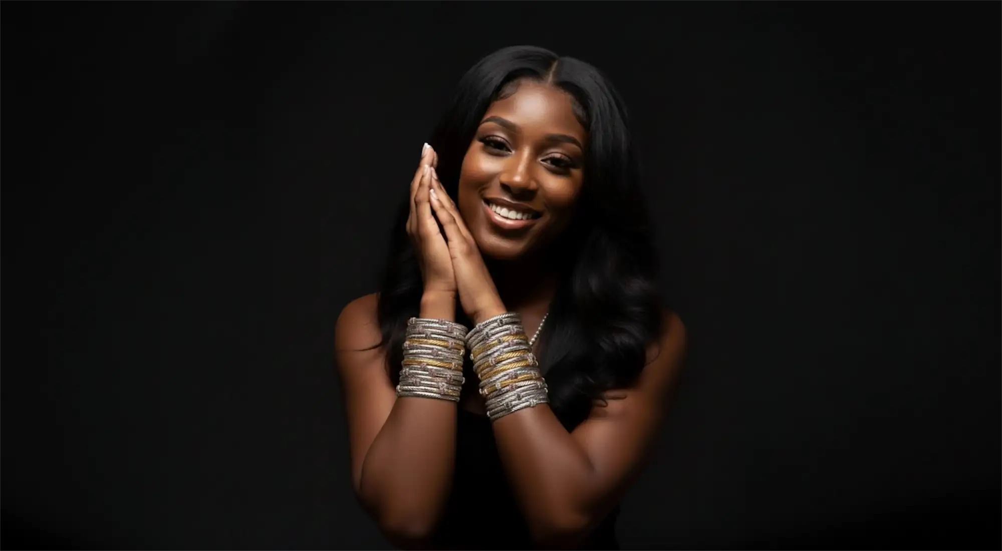 A woman wearing multiple stacked silver and gold-toned bangles on her wrists.